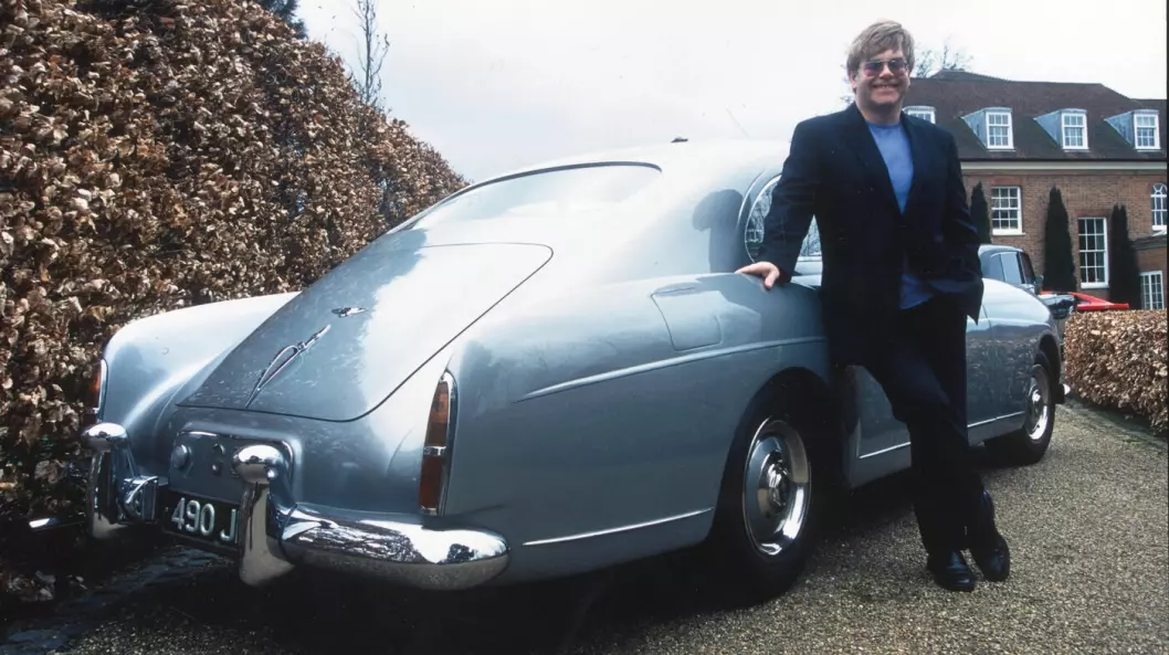 <span class="font-weight-bold" data-lab-font_weight_desktop="font-weight-bold">ALT OM ELTON: </span>Elton John poserer ved hofta til sin 1960-modell Bentley coupé. En av verdens mest berømte musikkartister skjøttet lenge en morsom, variert samling klassiske biler. Nå har han solgt flere unna på auksjon.