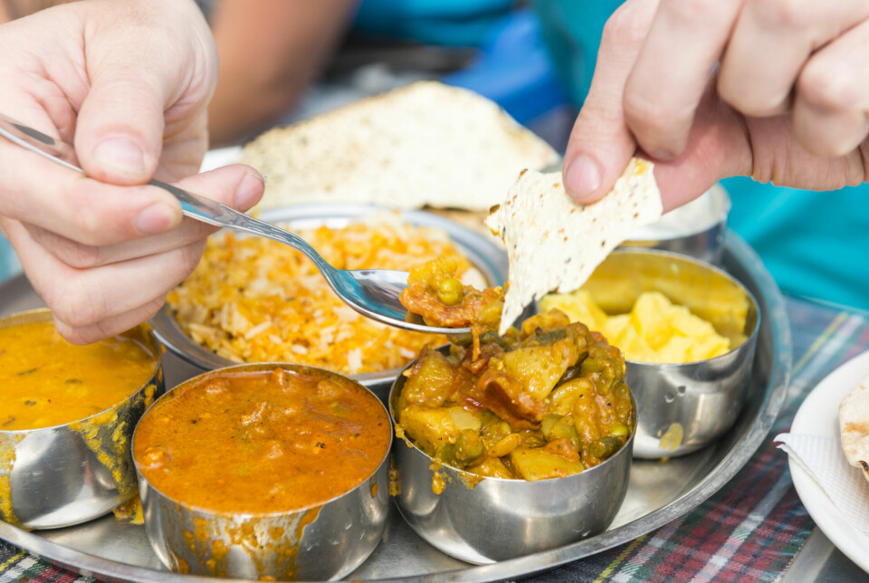 Eating traditional indian food Thali with hands and spoon. Visible just hands and palte with five different bowls with food.