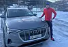 Person står ved en grå Audi e-tron parkert på snødekt plass i vinterlandskap.